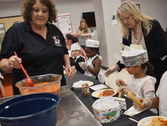 Candy Biehle (left), Smithville ISD child nutrition director, serves results of a food demonstration to elementary students in Smithville March 22. Superintendent Cheryl Burns assists at right. Photo by Fernando Castro